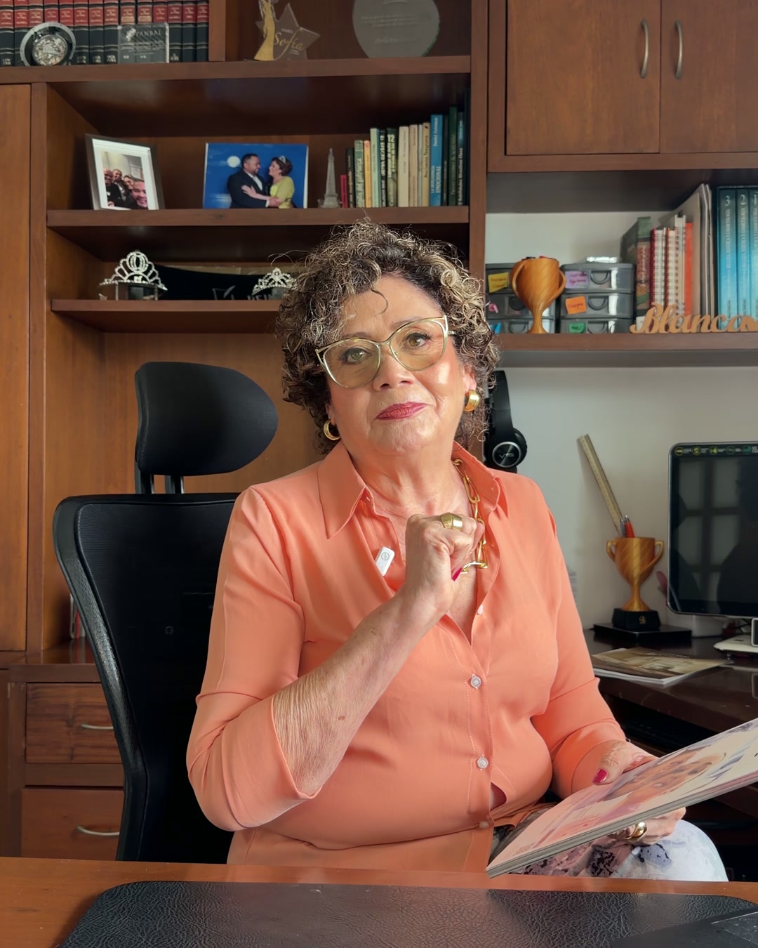 Blanca Inés Toro en su oficina, con el catálogo Yanbal en la mano y sus reconocimientos en la biblioteca